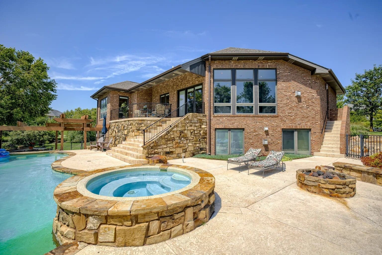 Brick house with large windows, pool, and hot tub in the backyard under a clear sky.