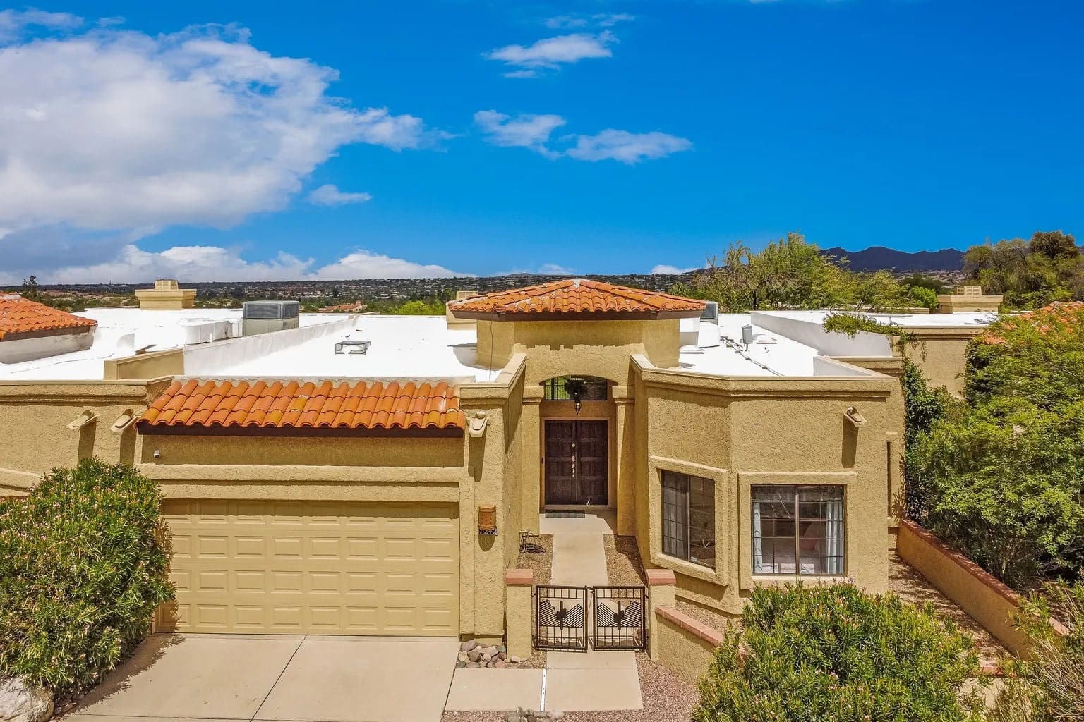 Single-story stucco house with red tile roof, garage, and desert landscaping under a blue sky.