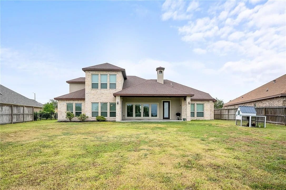 Large two-story house with a spacious backyard, surrounded by a wooden fence under a partly cloudy sky.