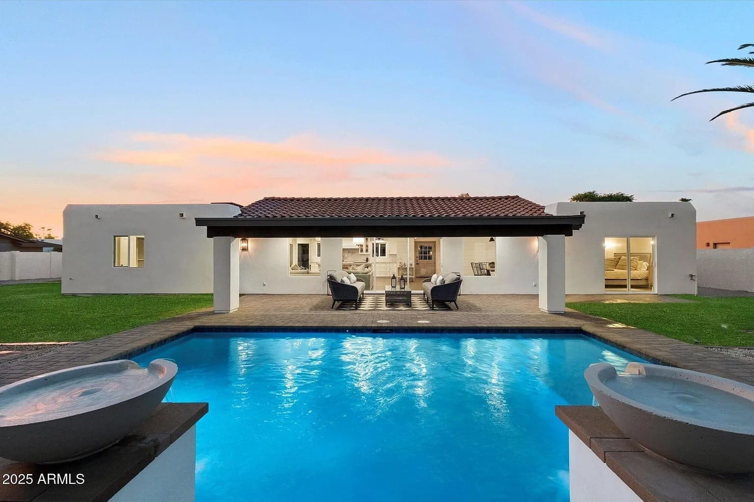 Modern white house with a tiled roof, pool in the foreground, and patio furniture under a pergola.
