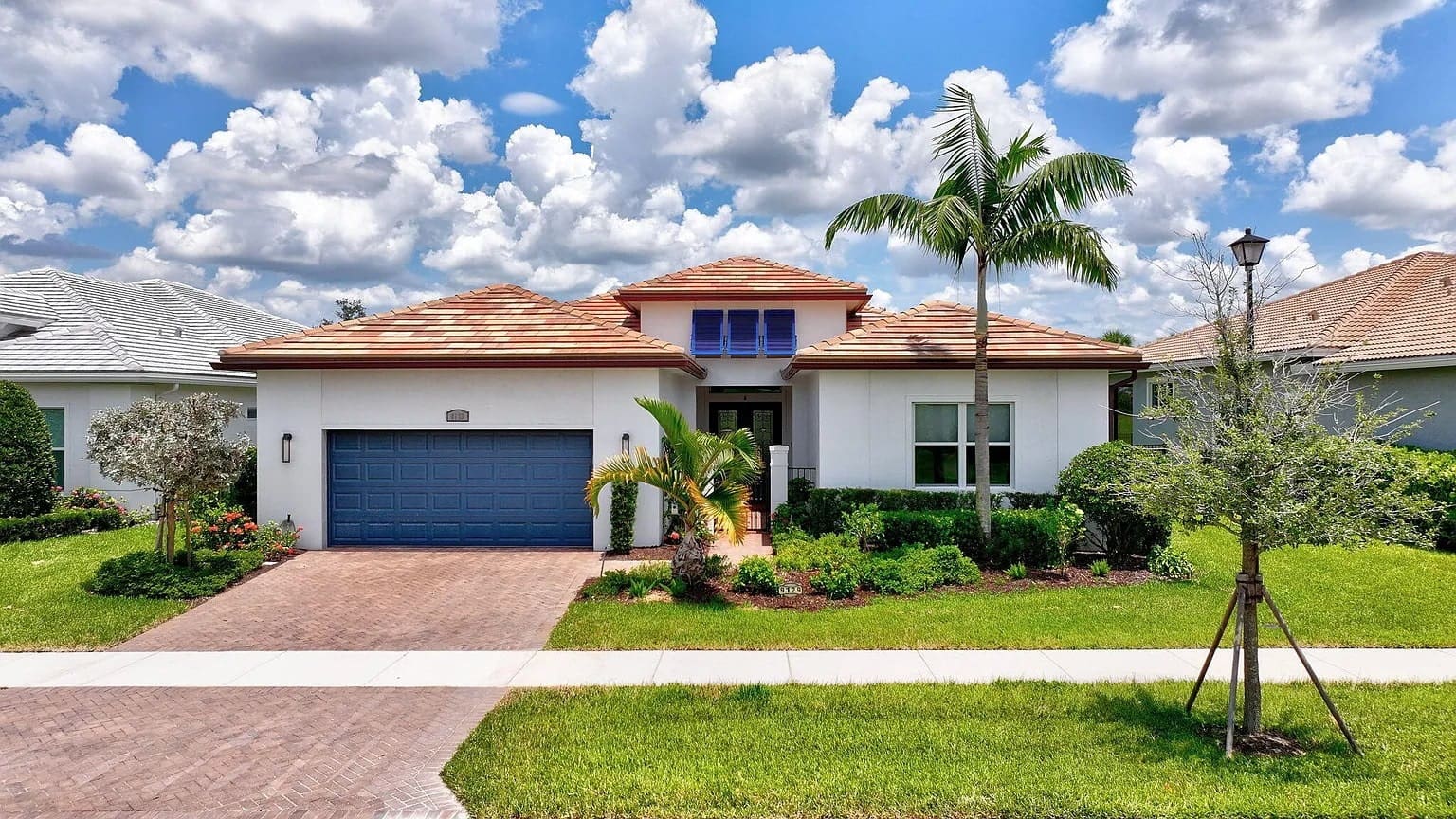 Single-story house with a red-tiled roof, blue garage door, and palm trees in front.