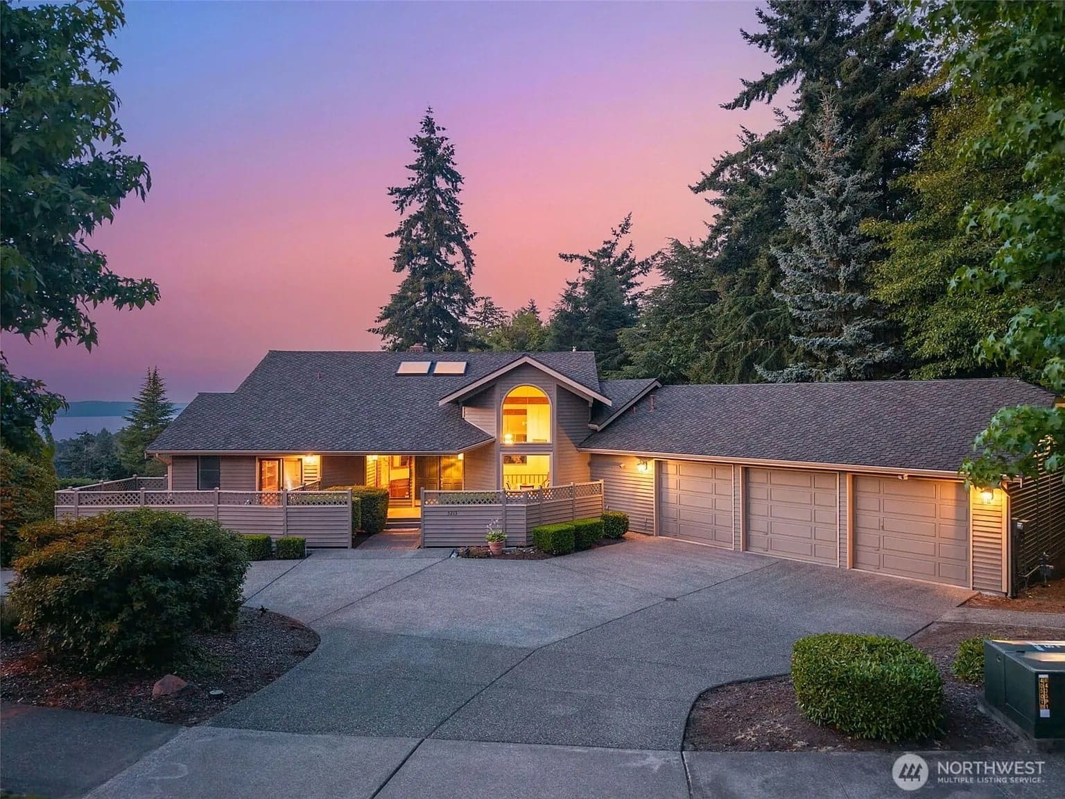 Single-story house with large garage, surrounded by trees, at sunset.