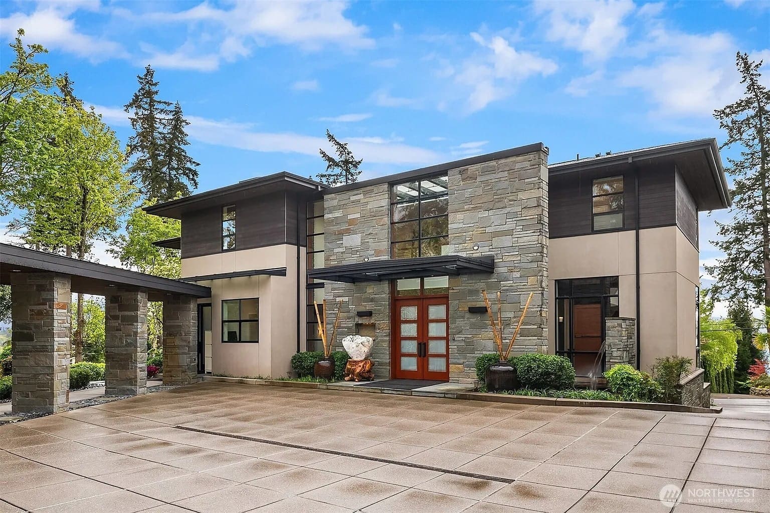 Modern two-story house with stone and wood facade, large windows, and a spacious driveway.