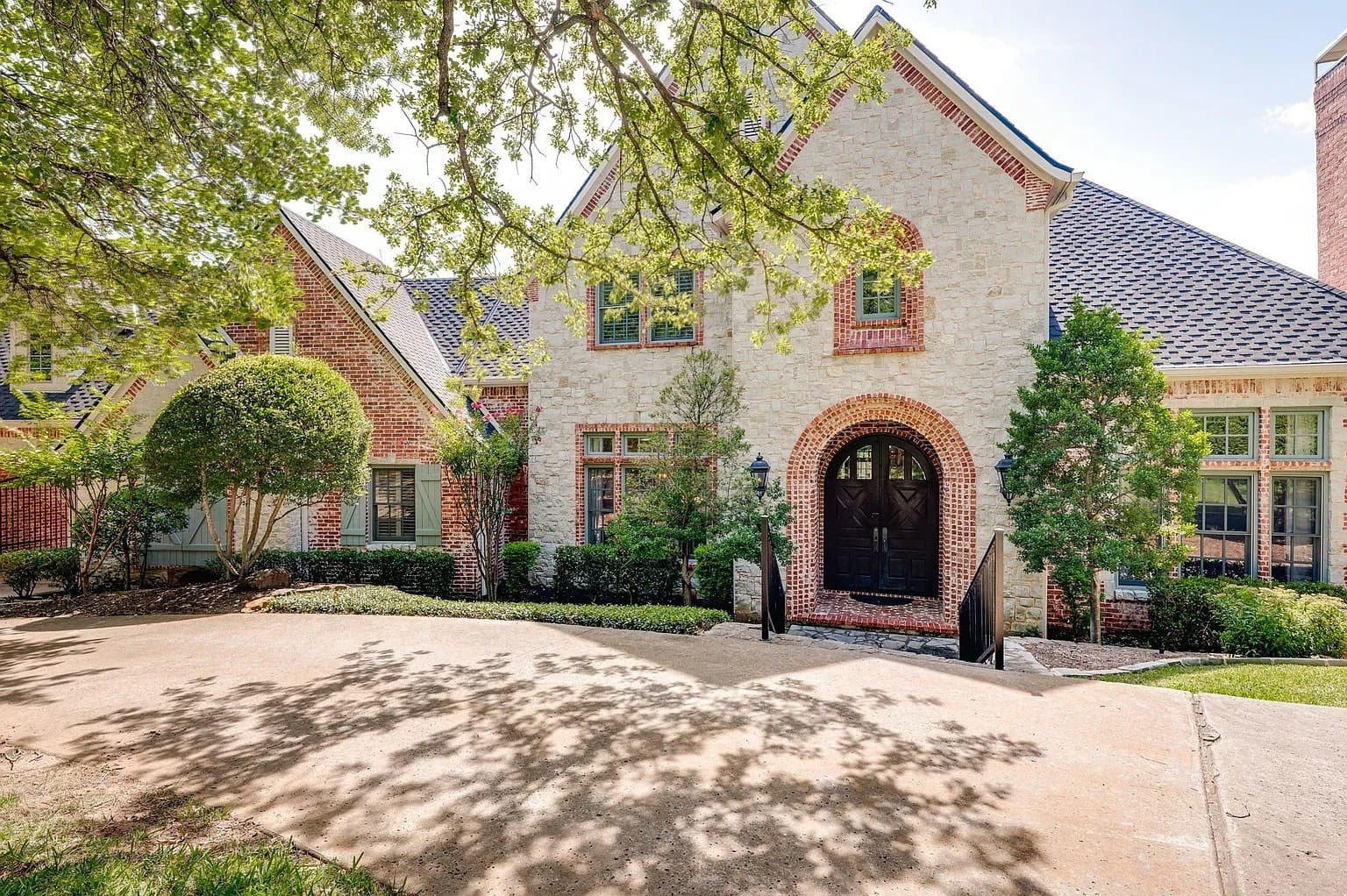 Large brick house with arched doorway, surrounded by trees and a spacious driveway.