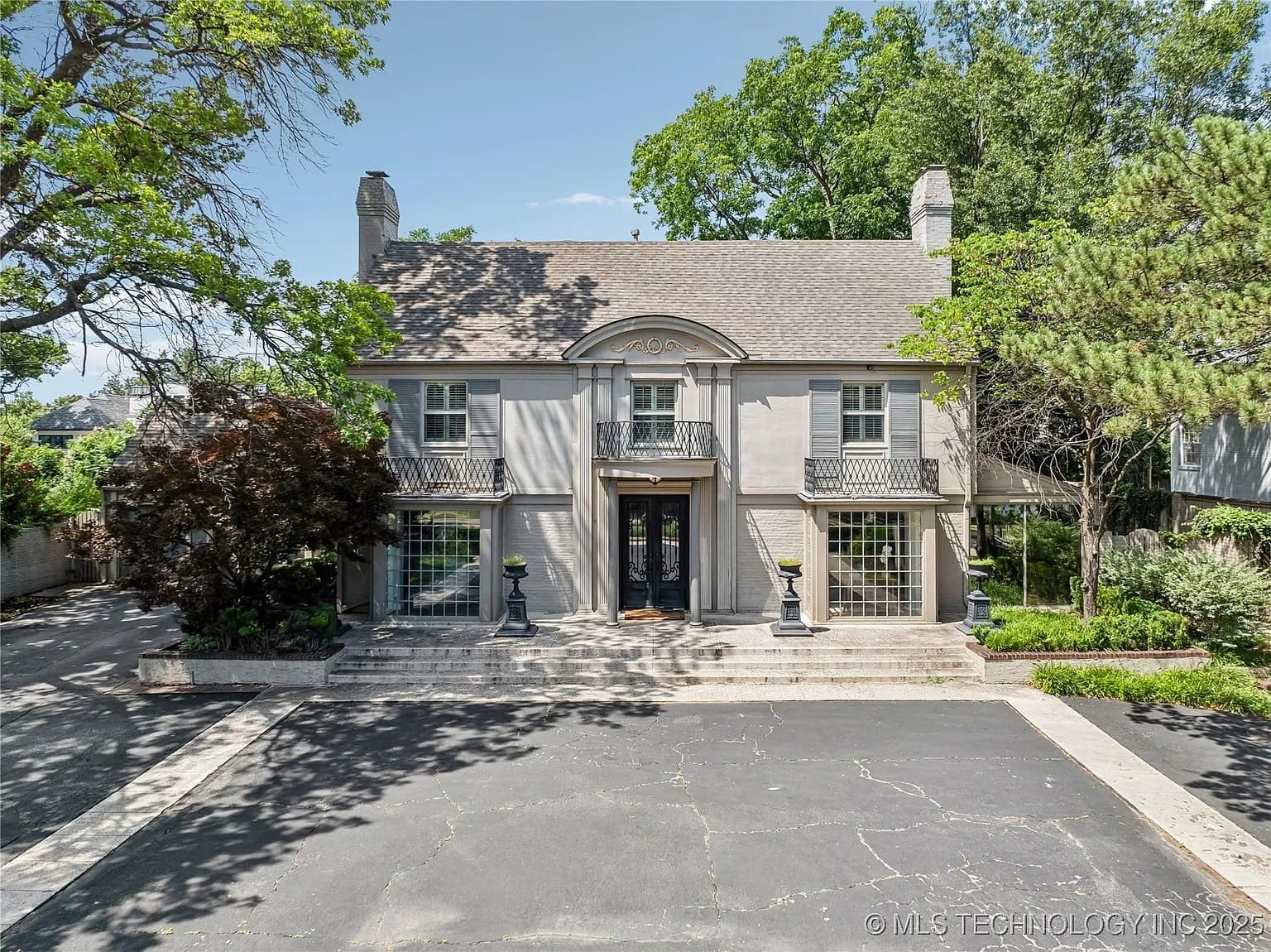 Two-story gray house with large windows, surrounded by trees and a paved driveway.