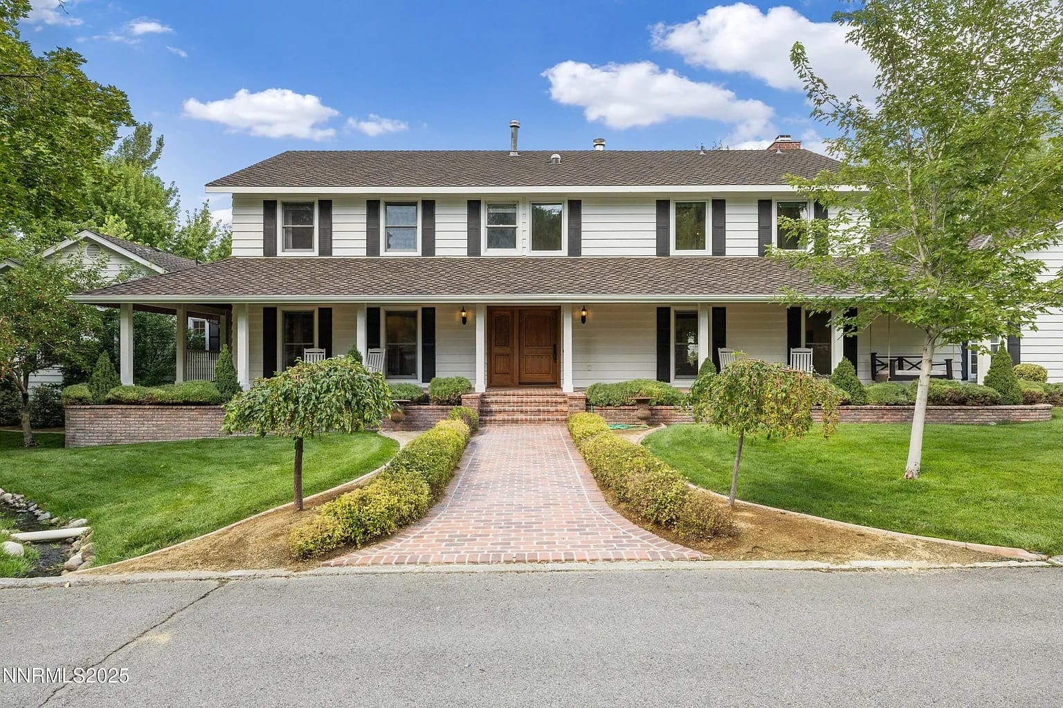Two-story white house with a large porch, brick walkway, and well-maintained lawn and trees.