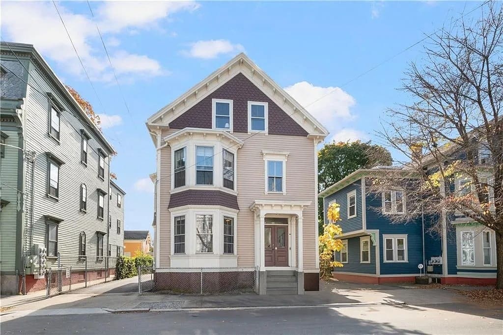 Victorian-style house with a pointed roof, flanked by two colorful neighboring homes.