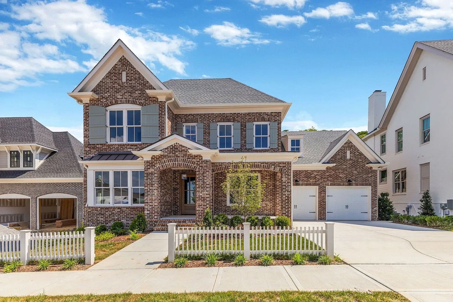 Two-story brick house with a white picket fence and attached garage under a blue sky.