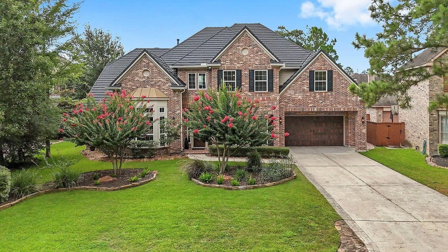 Two-story brick house with a manicured lawn, trees, and a concrete driveway.