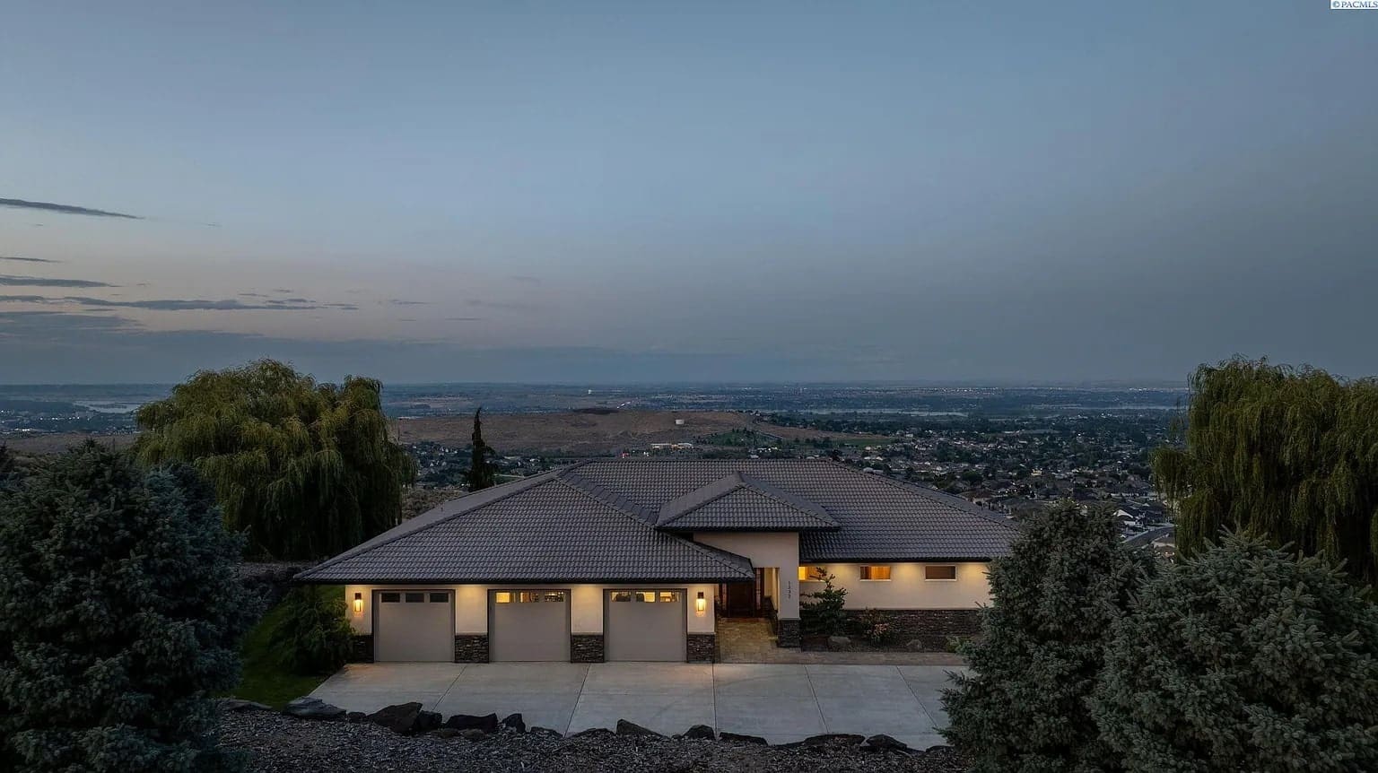 Single-story house with a three-car garage, set against a twilight cityscape and distant hills.