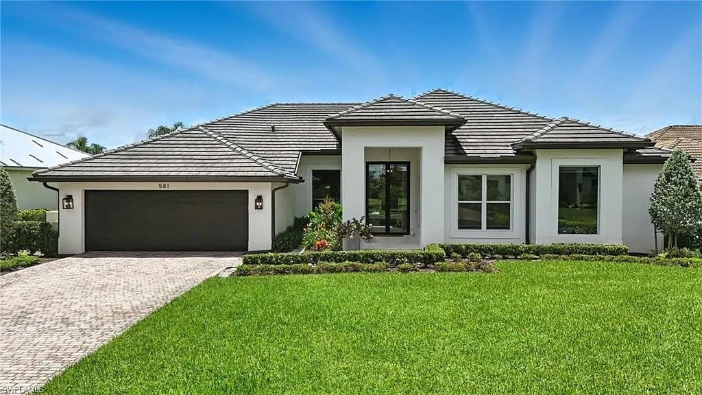 Modern single-story house with a dark garage, manicured lawn, and clear blue sky.
