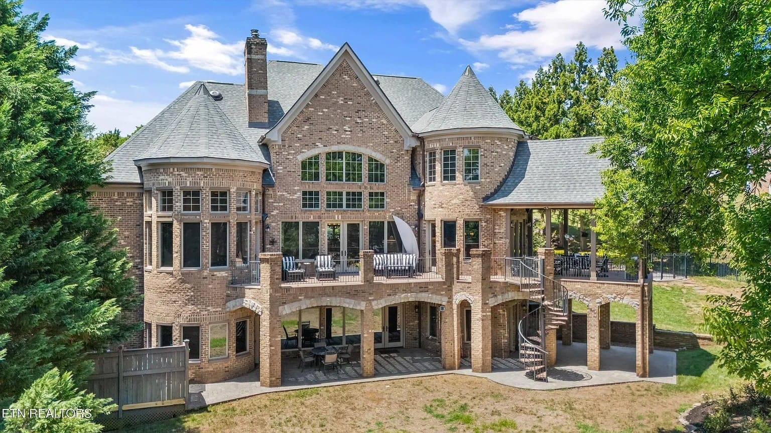 Large brick mansion with turrets, multiple windows, and a spiral staircase, surrounded by trees.