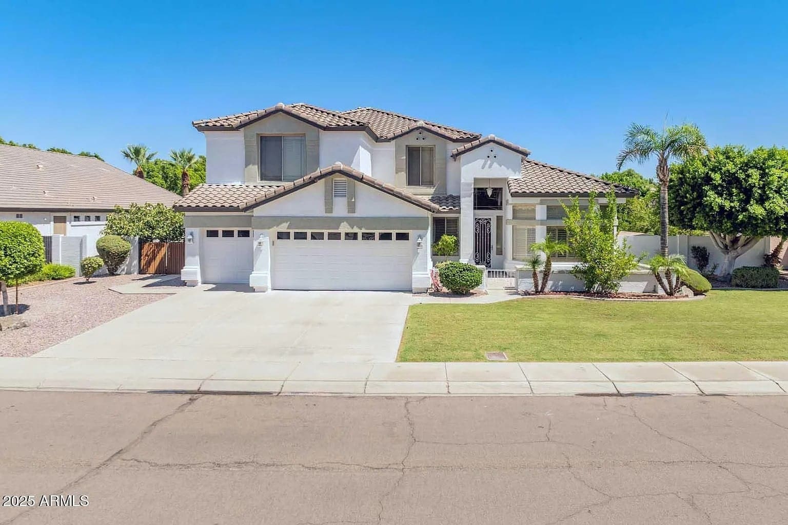 Two-story suburban house with a three-car garage, front lawn, and palm trees under a clear sky.
