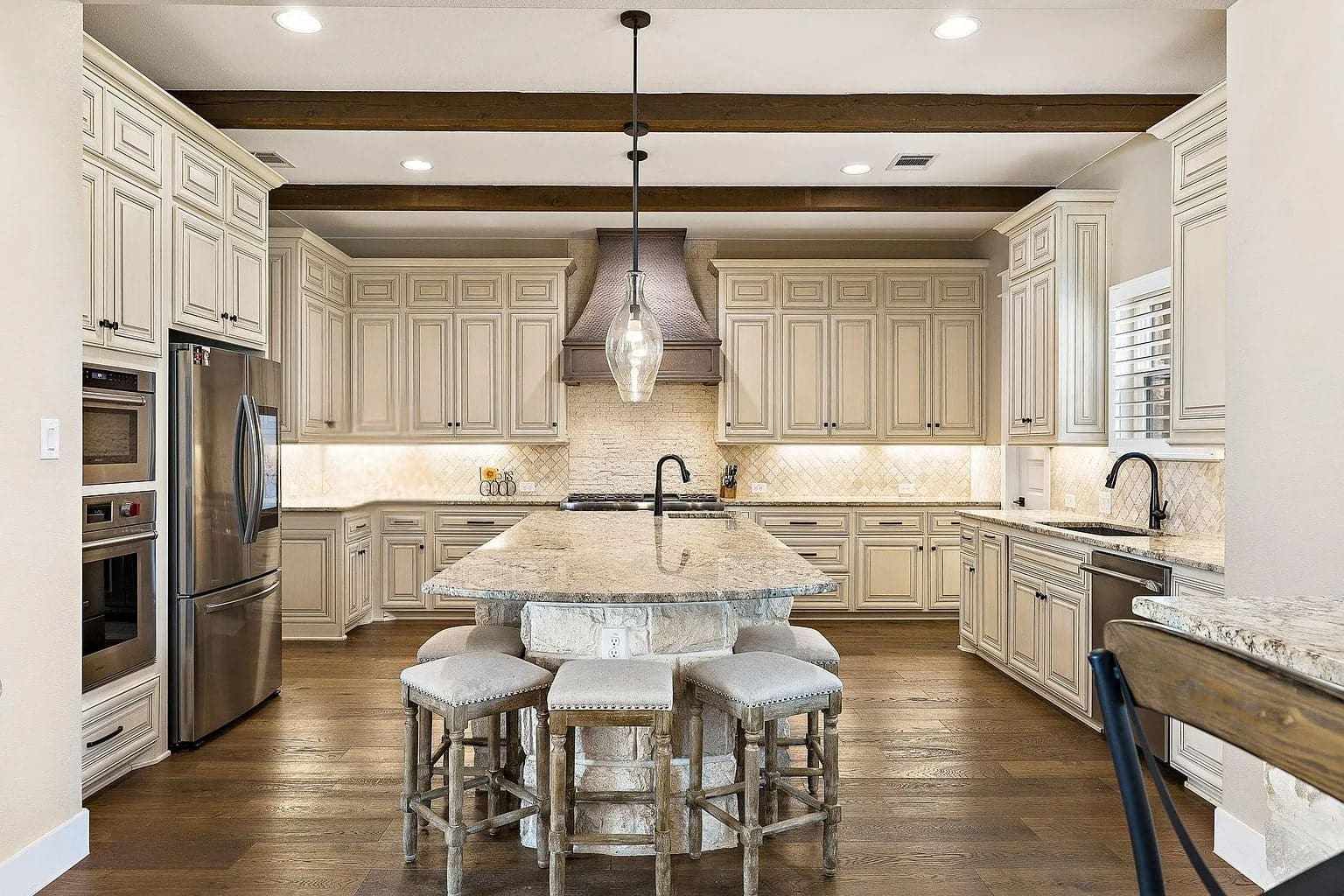 Spacious kitchen with beige cabinets, large island, stainless steel appliances, and wooden ceiling beams.