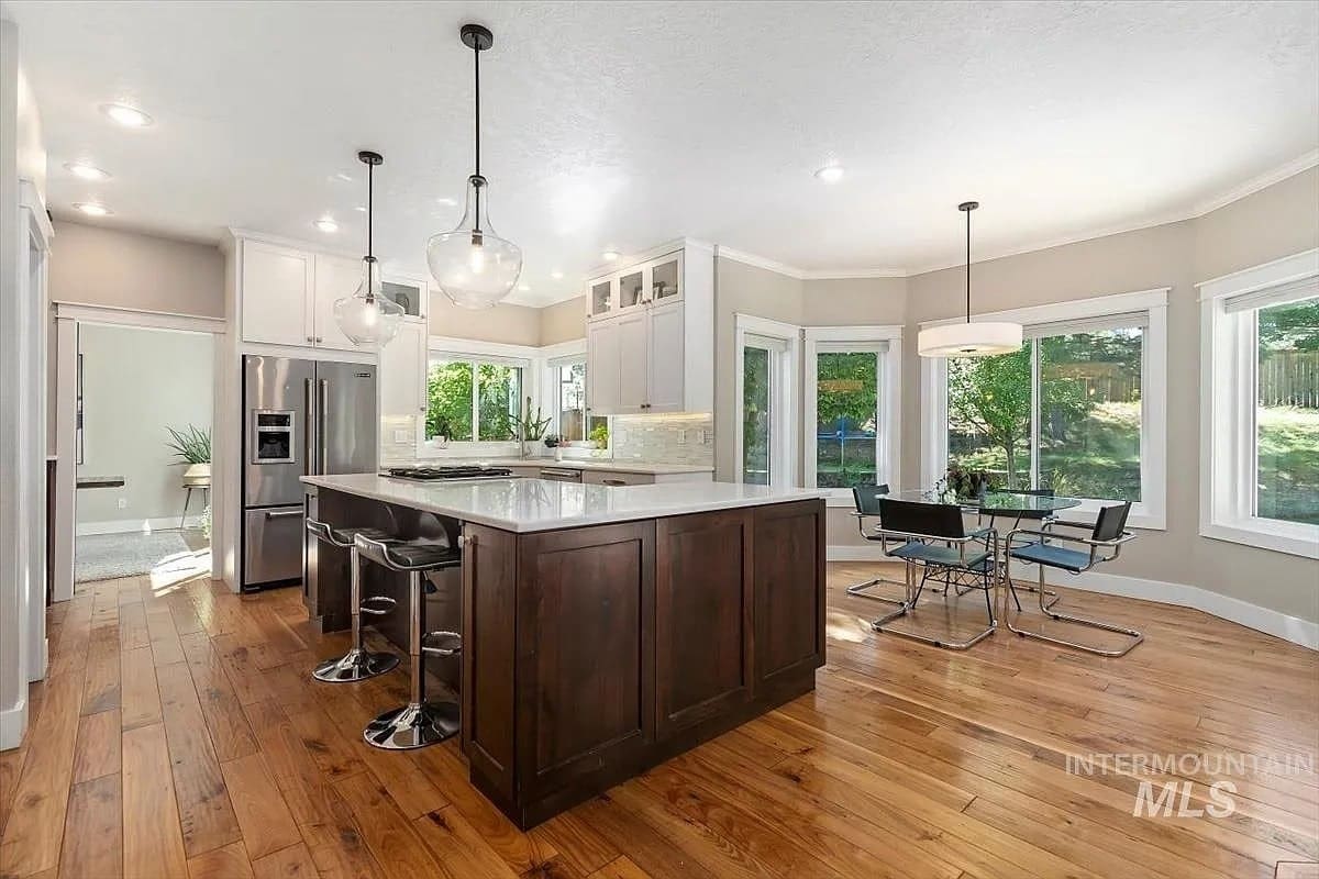 Modern kitchen with wooden floors, large island, pendant lights, and a dining area with garden view.