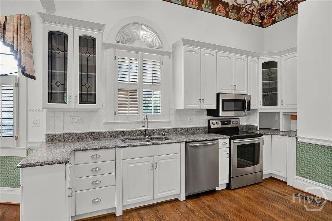 White kitchen with stainless steel appliances, granite countertops, and decorative glass cabinet doors.