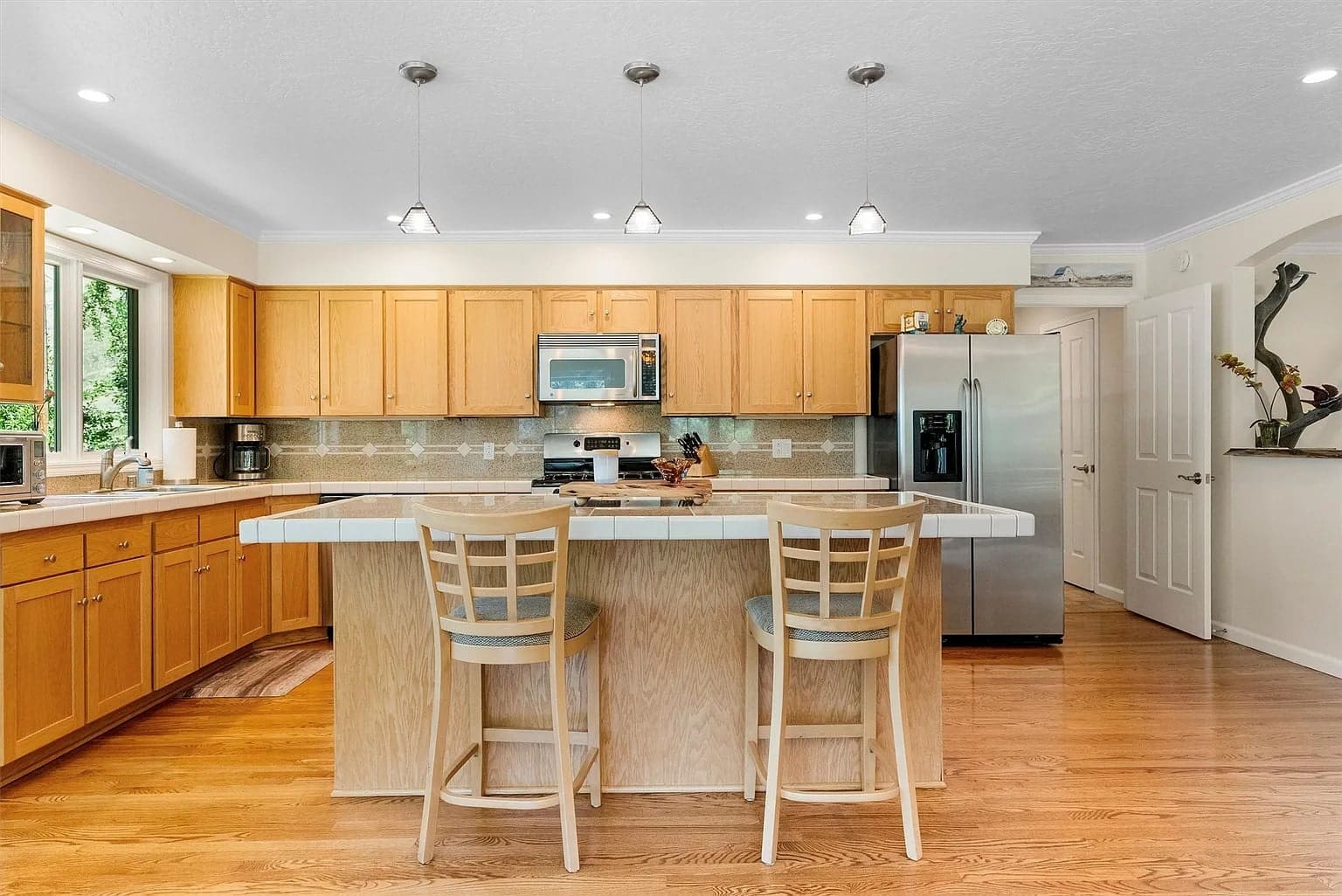 Spacious kitchen with wooden cabinets, island with two chairs, stainless steel appliances, and pendant lighting.