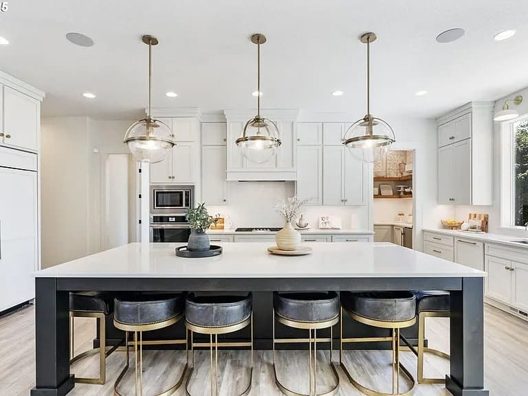 Modern kitchen with large island, pendant lights, and bar stools. White cabinets and stainless steel appliances.
