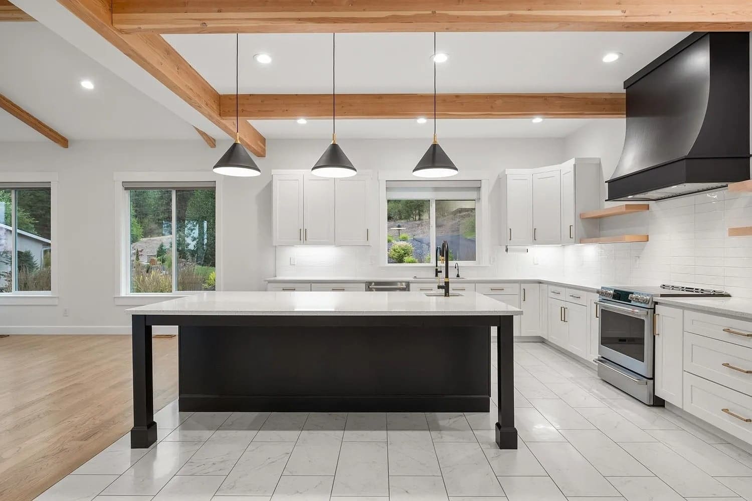Modern kitchen with white cabinets, large island, pendant lights, and wooden beams on the ceiling.