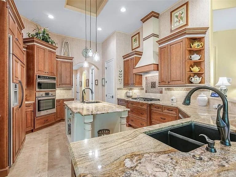Spacious kitchen with wooden cabinets, granite countertops, island, and modern appliances. Warm lighting and decor.
