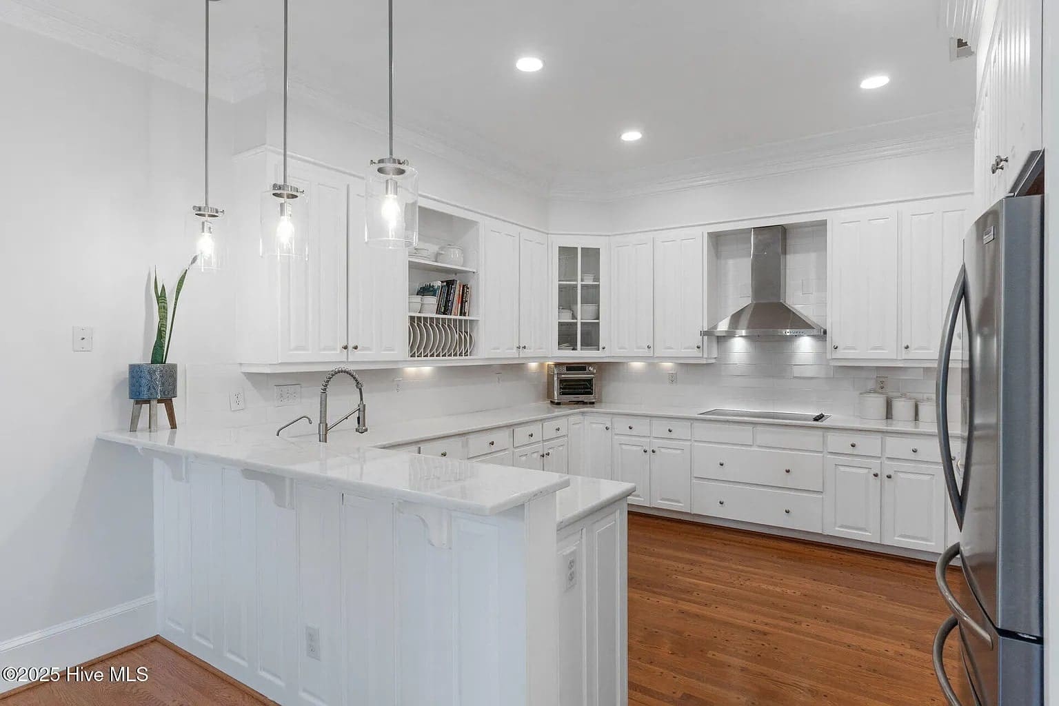 Modern kitchen with white cabinets, stainless steel appliances, pendant lights, and wooden flooring.
