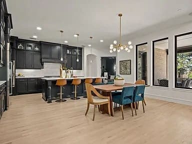 Modern kitchen and dining area with black cabinets, island seating, wooden table, and large windows.