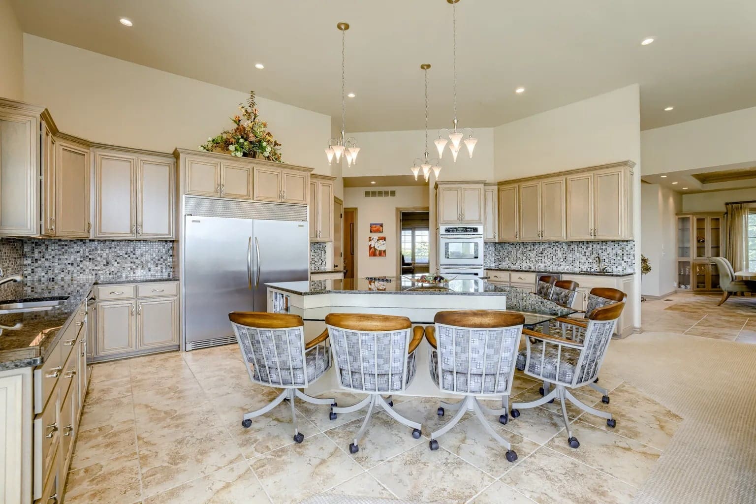 Spacious kitchen with a large island, eight chairs, modern appliances, and tiled flooring.