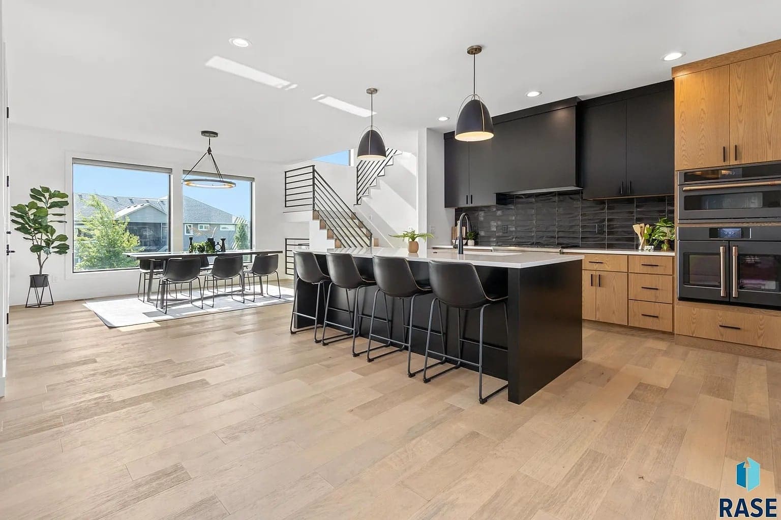 Modern kitchen and dining area with black and wood cabinetry, island seating, and large windows.