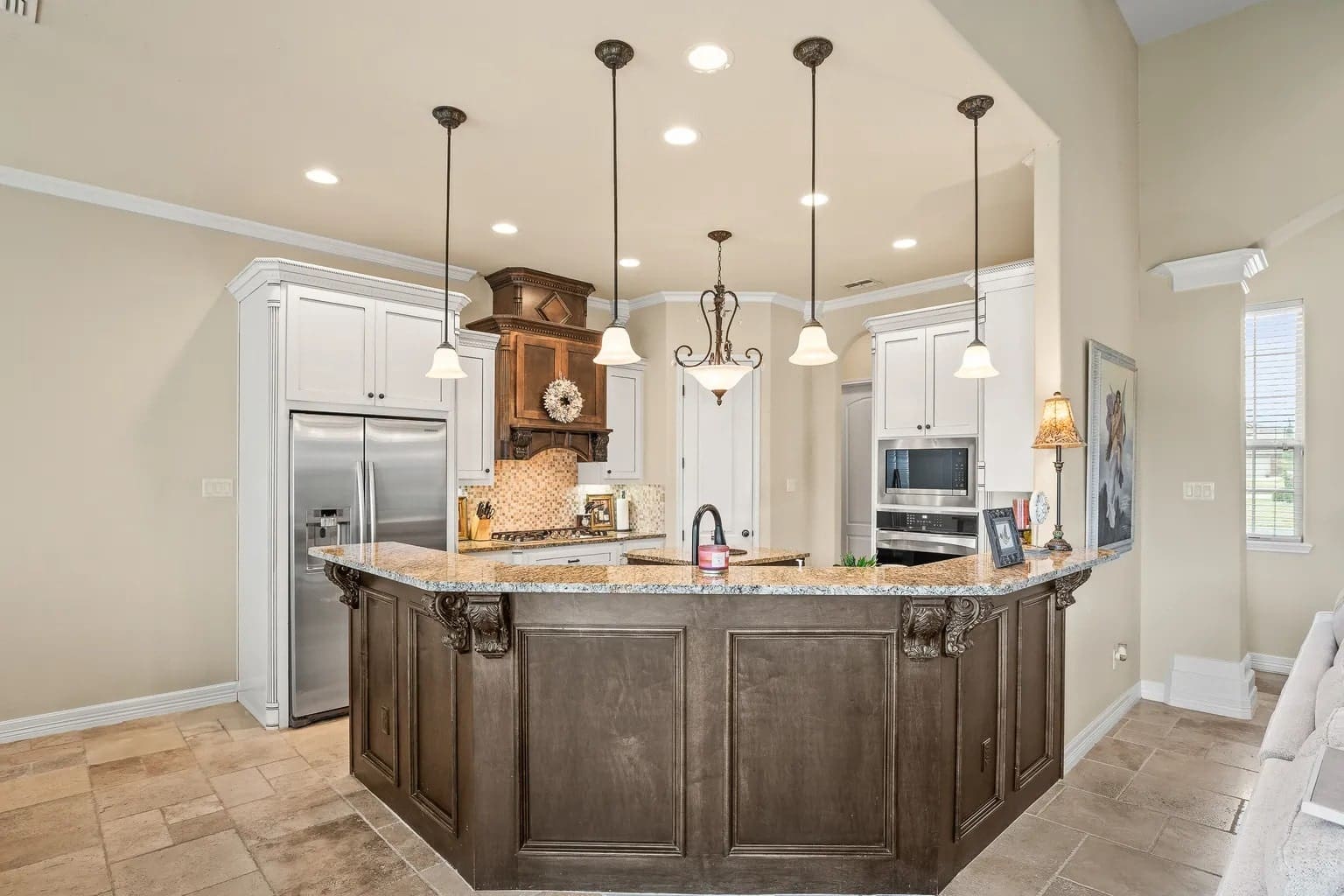 Modern kitchen with a central island, pendant lighting, stainless steel appliances, and beige tile flooring.