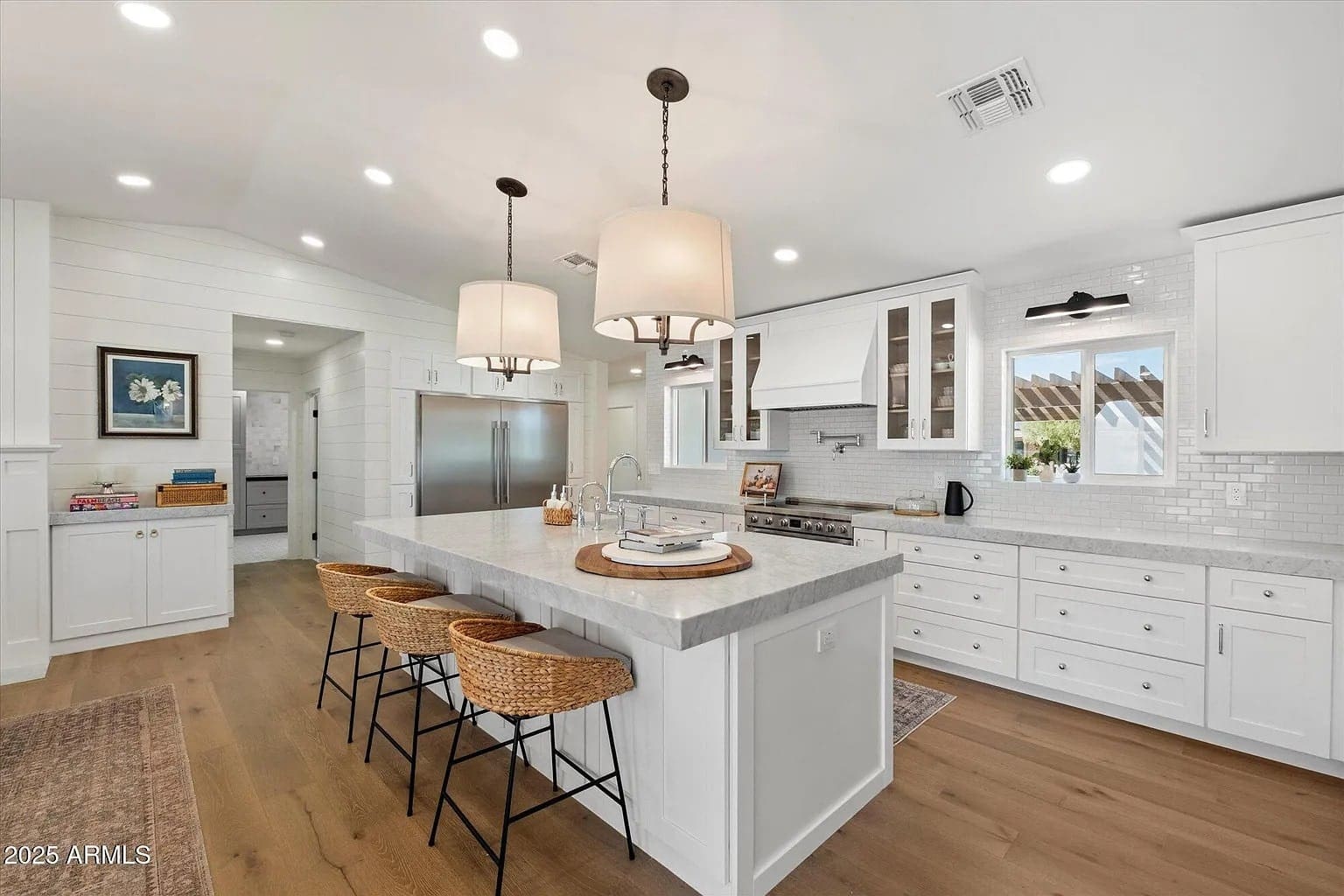 Modern kitchen with white cabinets, marble island, wicker stools, and pendant lights. Bright and spacious.