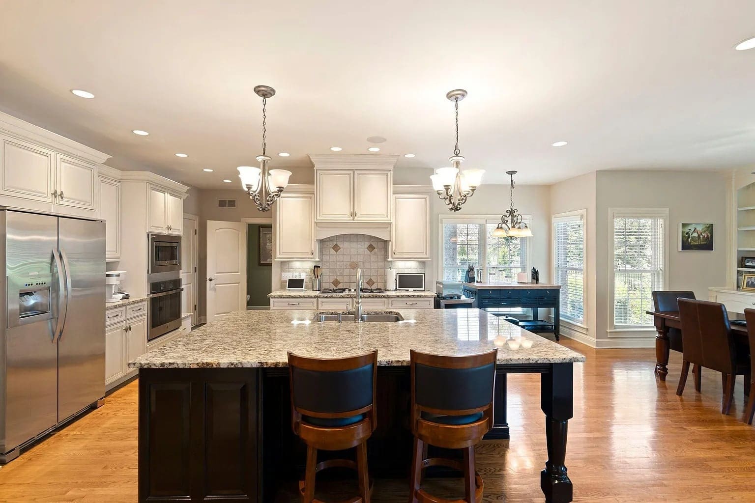 Spacious kitchen with granite island, stainless steel appliances, white cabinets, and hardwood floors.
