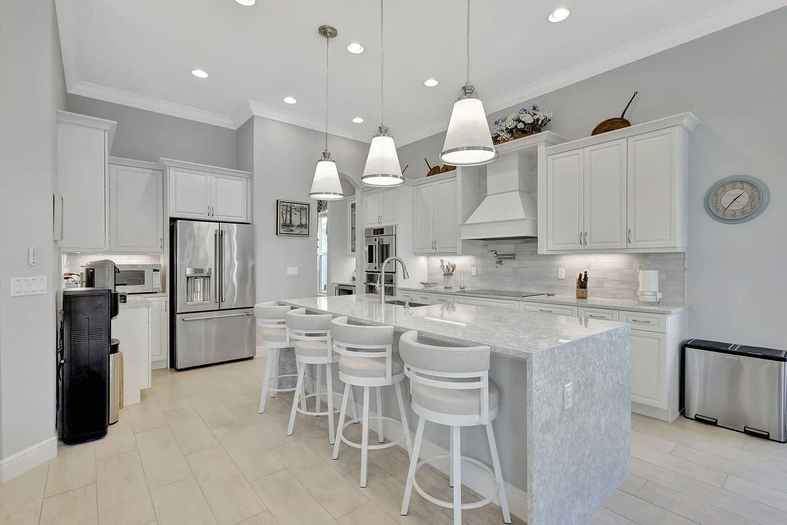 Modern kitchen with white cabinets, marble island, stainless steel appliances, and pendant lighting.