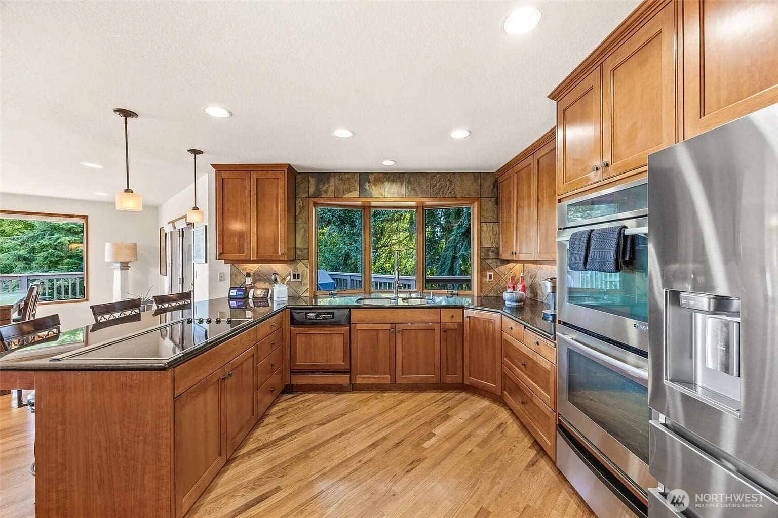 Spacious kitchen with wooden cabinets, stainless steel appliances, and large windows overlooking greenery.