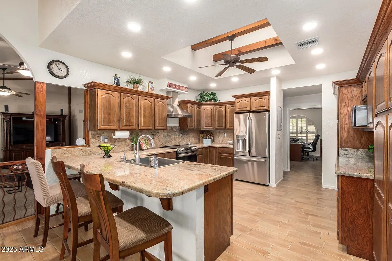 Spacious kitchen with wooden cabinets, marble countertops, stainless steel appliances, and bar seating.