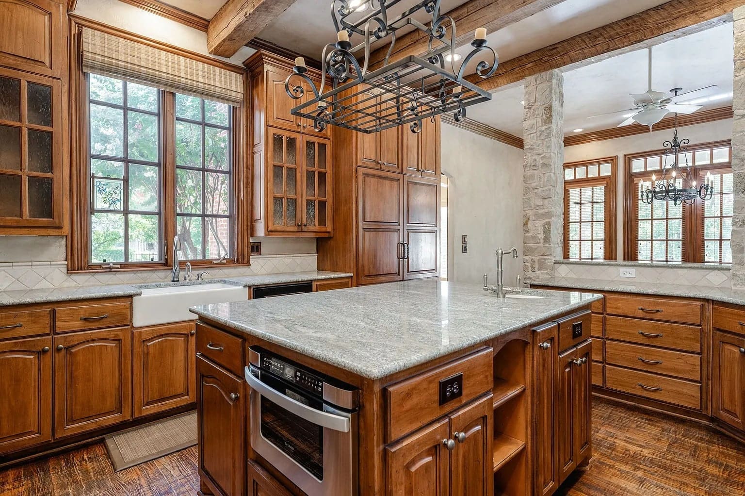 Spacious kitchen with wooden cabinets, large island, granite countertops, and a hanging pot rack.