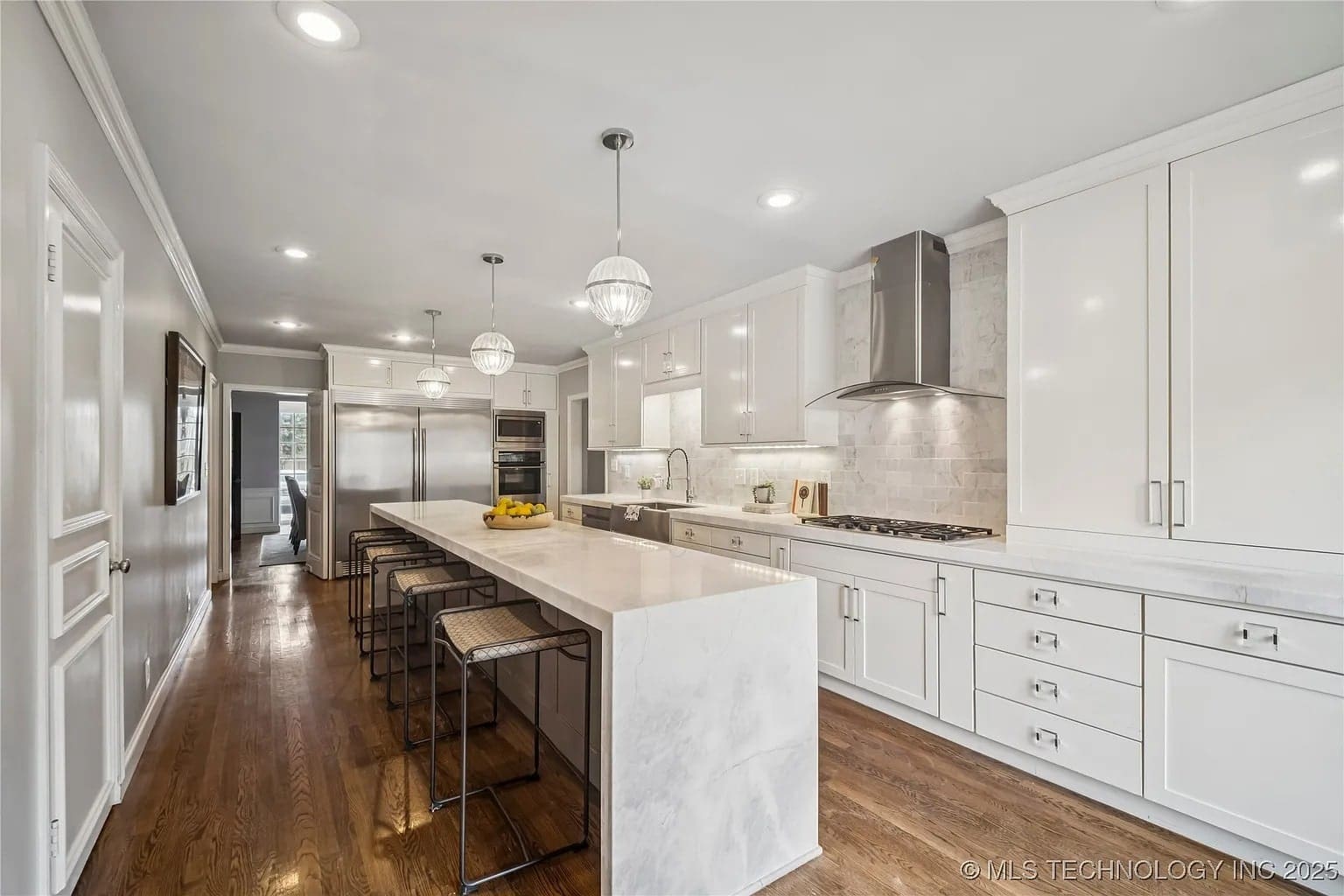 Modern kitchen with white cabinets, marble island, stainless steel appliances, and wooden floor.