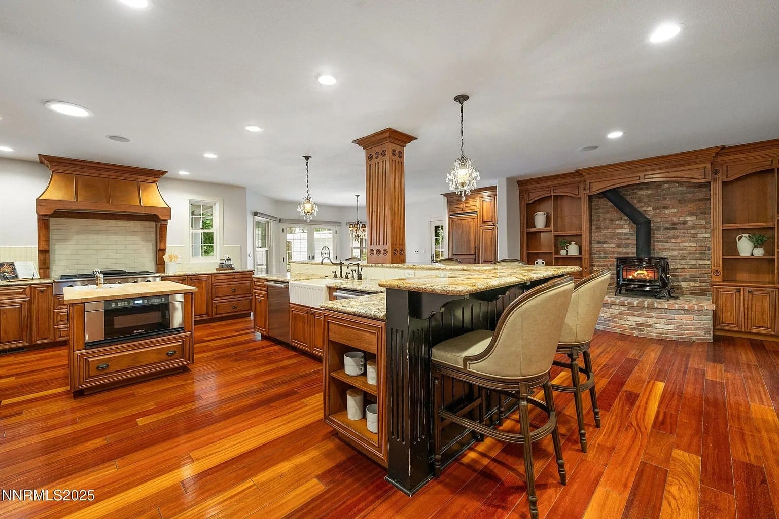 Spacious kitchen with wooden flooring, island, bar seating, and a brick fireplace.