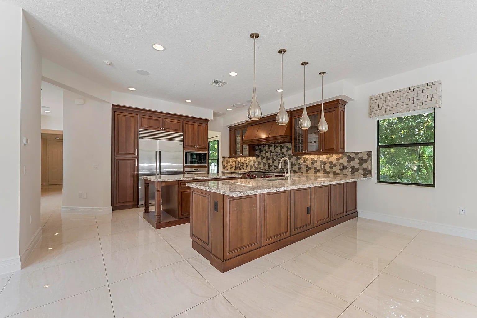 Spacious modern kitchen with wooden cabinets, marble countertops, pendant lights, and stainless steel appliances.