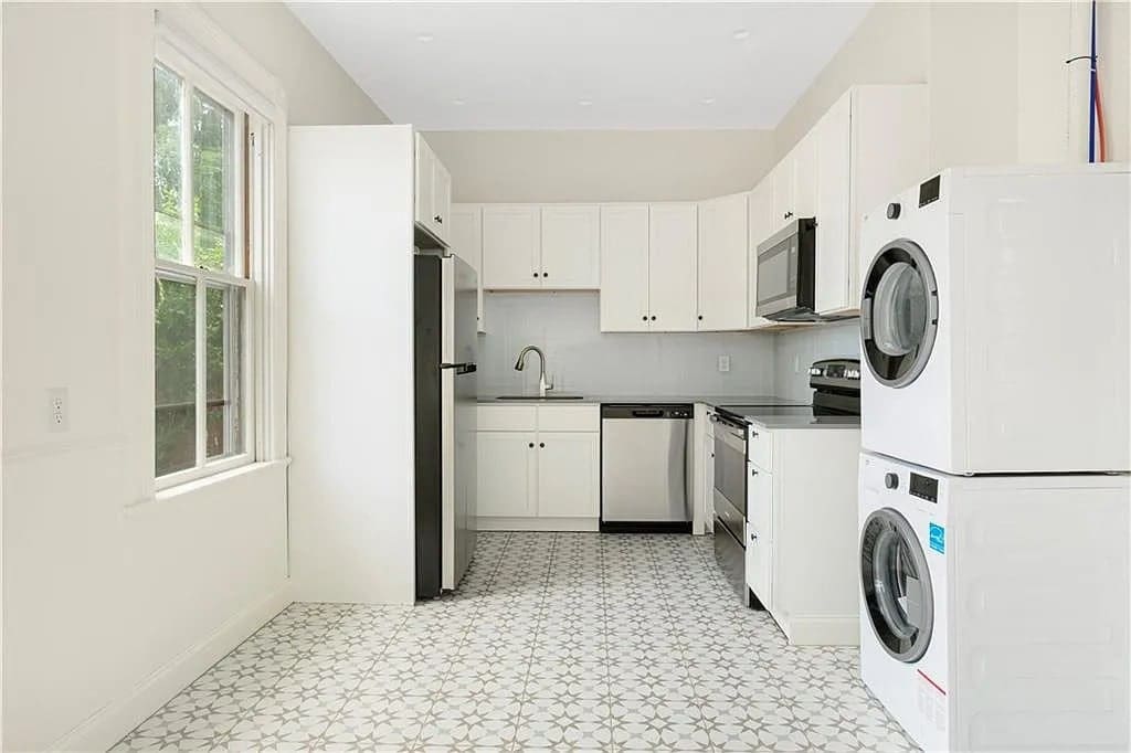 Modern kitchen with white cabinets, stainless steel appliances, and stacked washer and dryer.