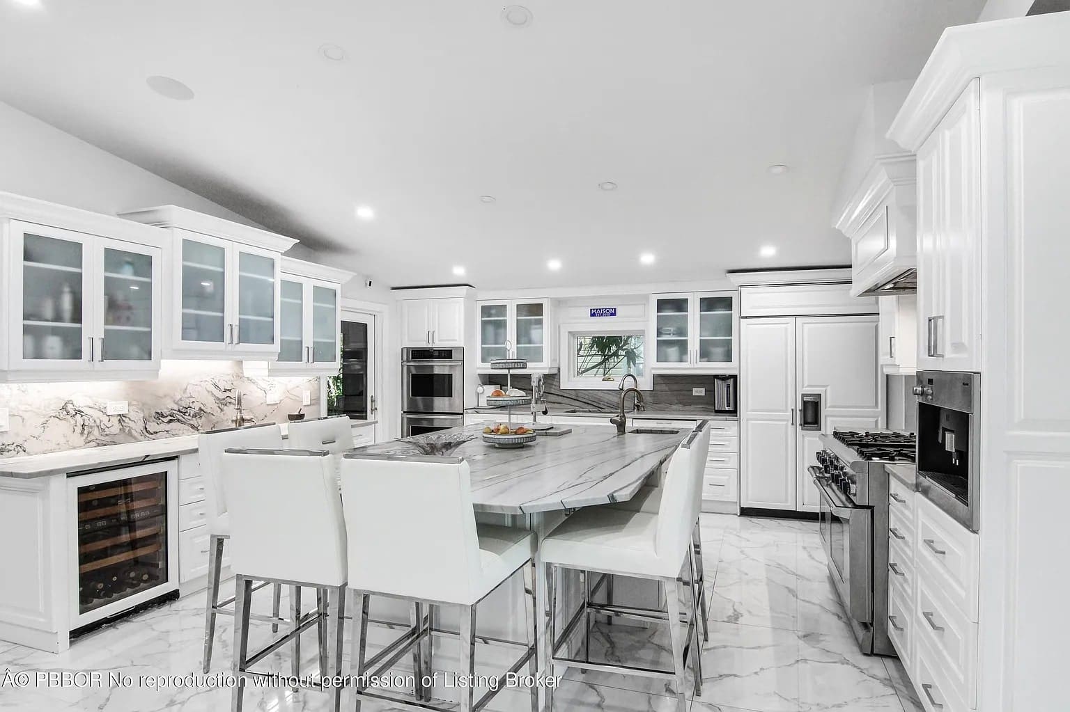 Modern kitchen with white cabinets, marble countertops, island seating, and stainless steel appliances.