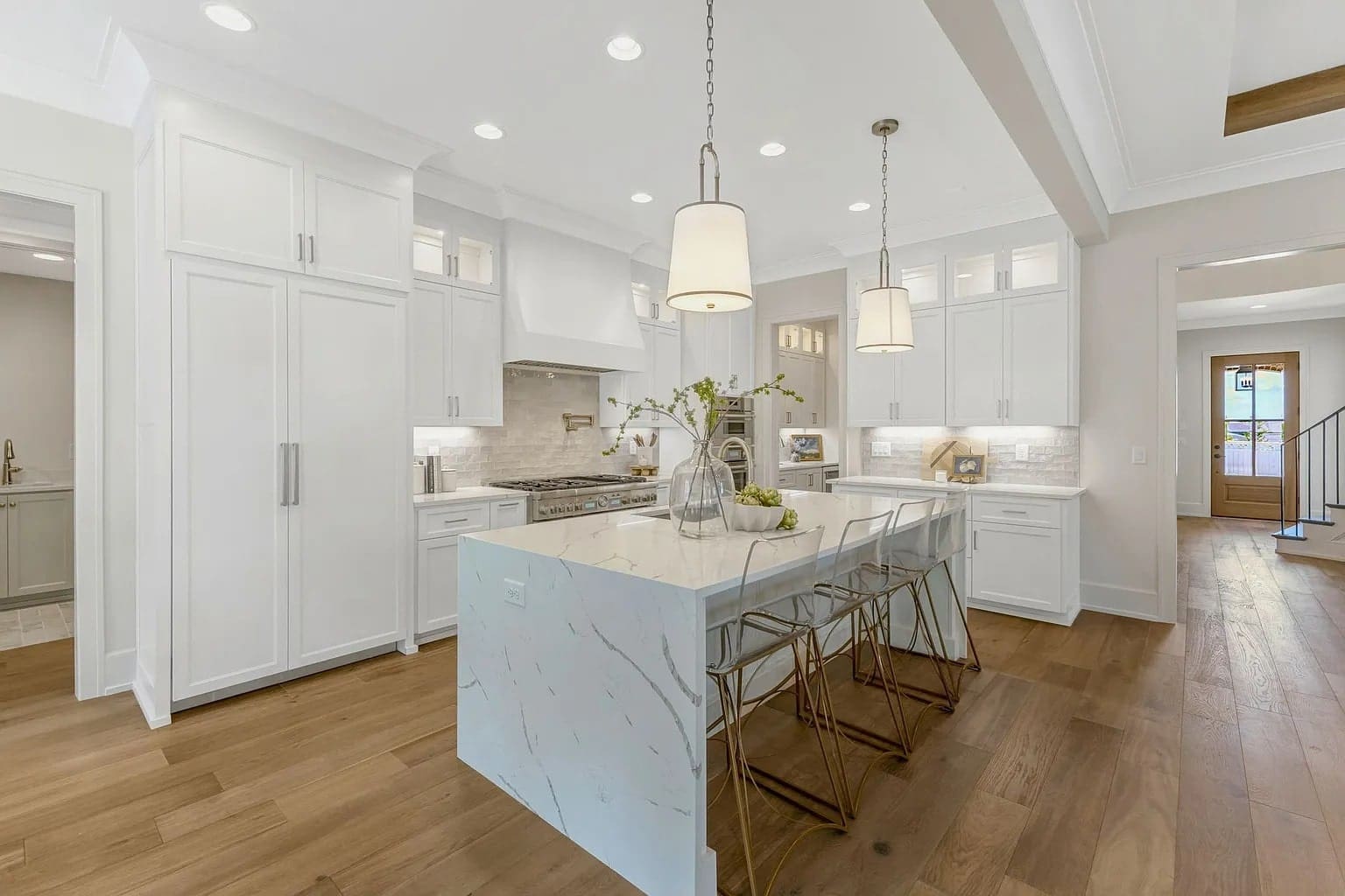 Modern kitchen with white cabinets, marble island, pendant lights, and wooden flooring.