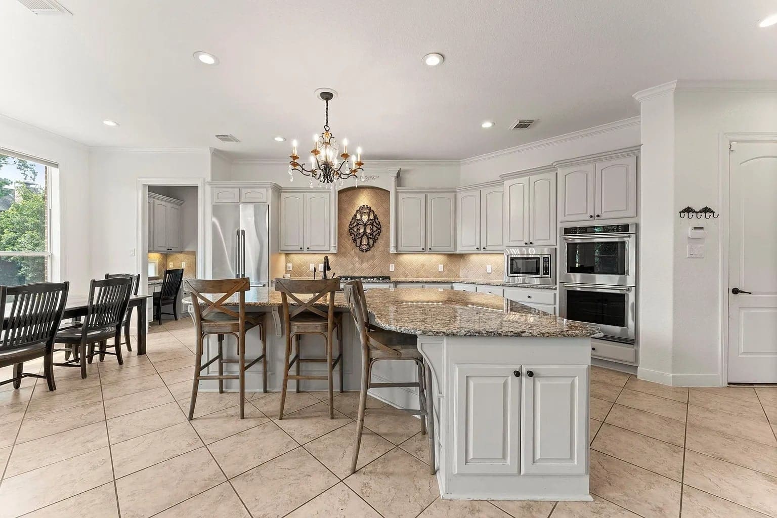 Spacious kitchen with white cabinets, granite countertops, island seating, and a chandelier. Dining area visible.