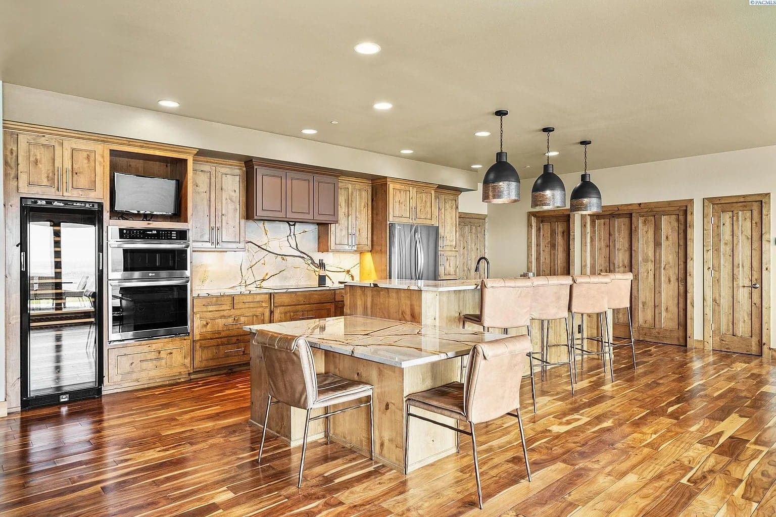 Spacious kitchen with wooden cabinets, marble countertops, island, and modern pendant lights.