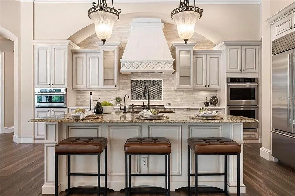 Spacious kitchen with a large island, barstools, pendant lights, and stainless steel appliances.