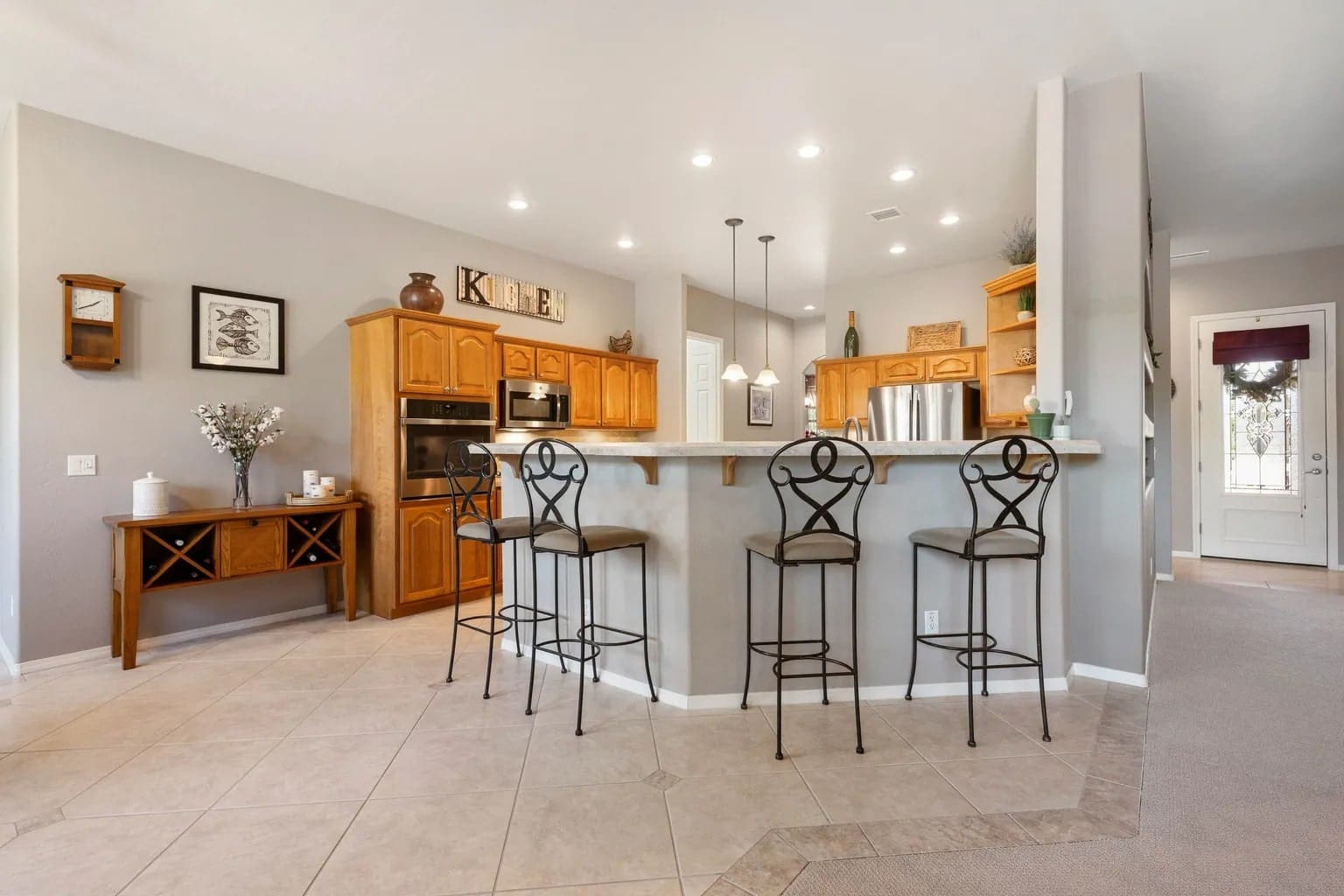 Spacious kitchen with wooden cabinets, bar counter, and four metal bar stools.