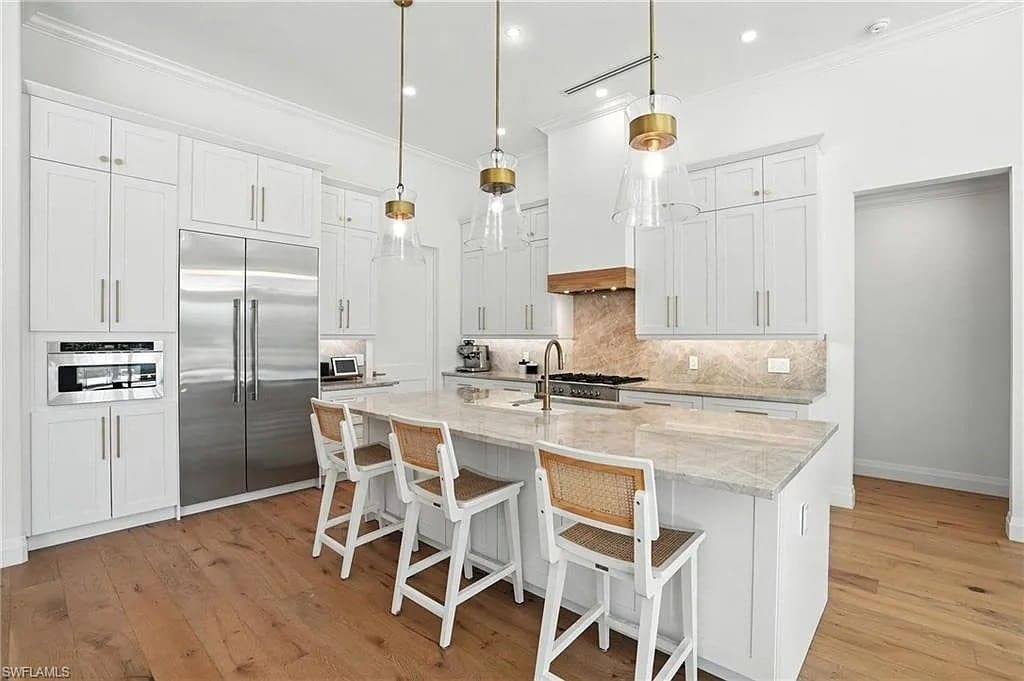 Modern kitchen with white cabinets, marble island, pendant lights, and wooden bar stools.