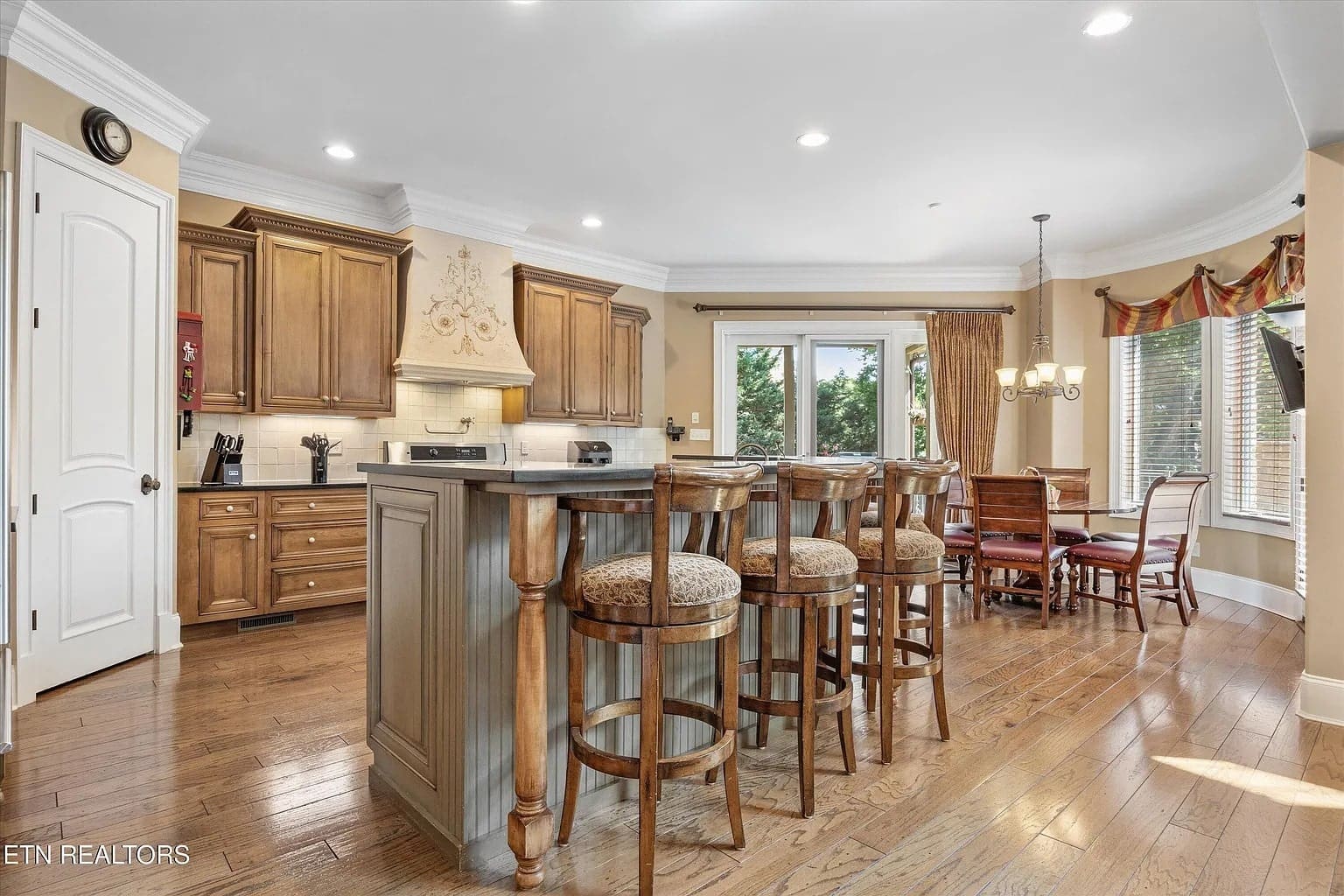 Spacious kitchen with wooden cabinets, island with bar stools, dining area, and large windows.