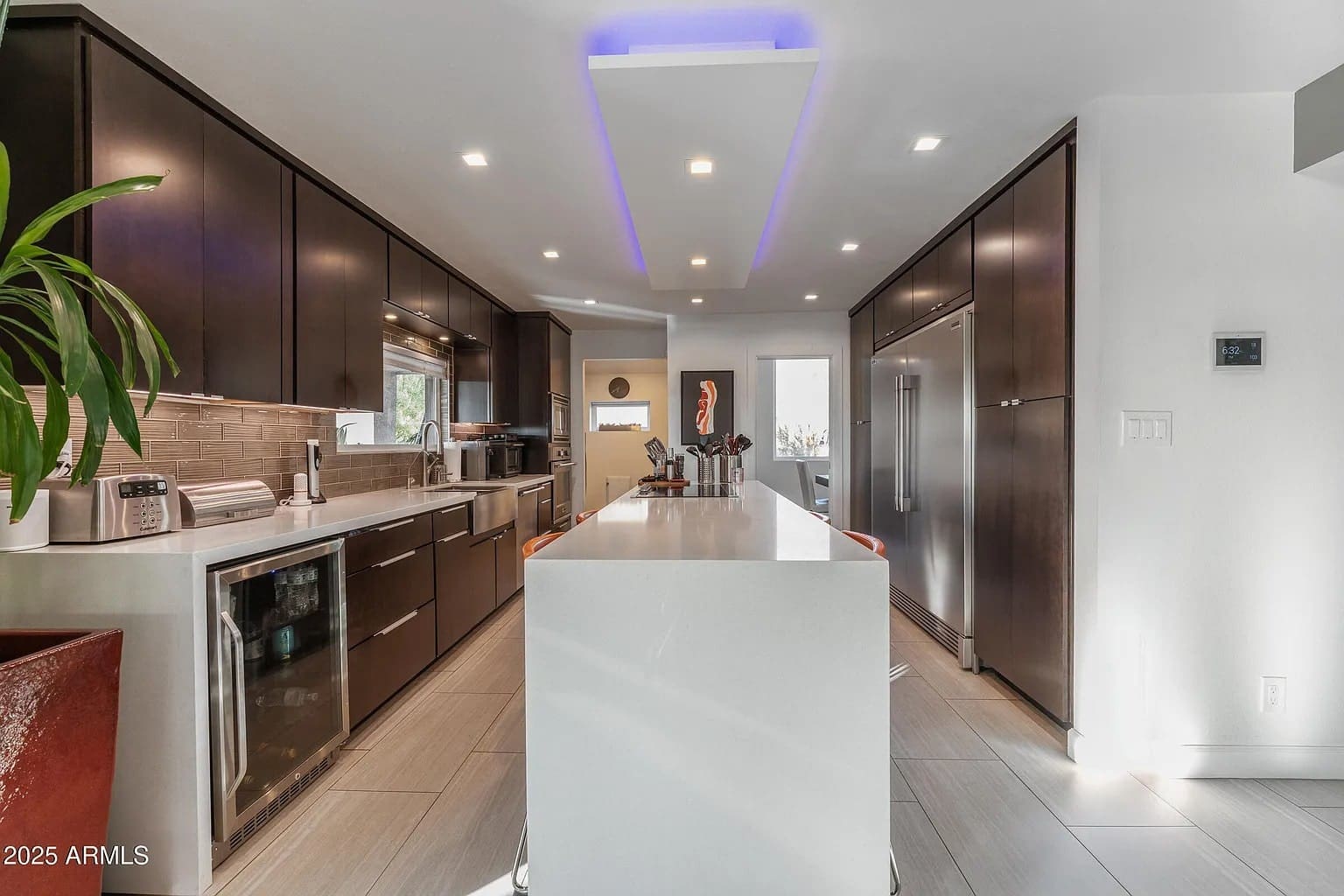 Modern kitchen with dark cabinets, white island, stainless steel appliances, and recessed lighting.