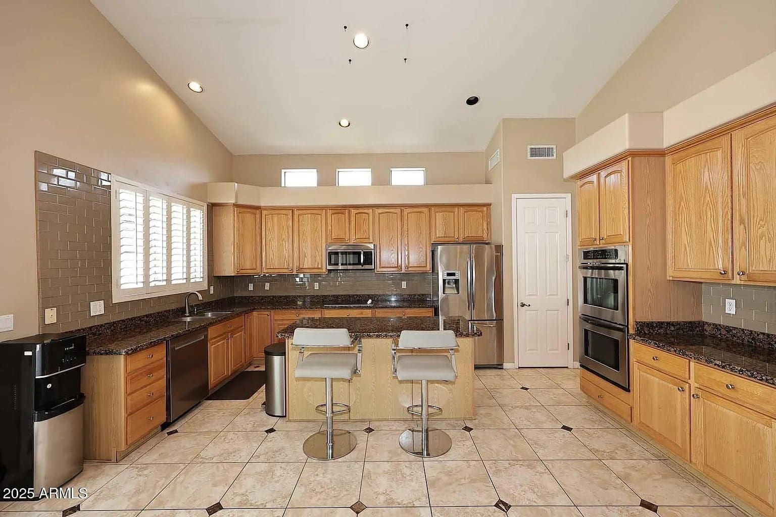 Spacious kitchen with wooden cabinets, granite countertops, stainless steel appliances, and two bar stools.