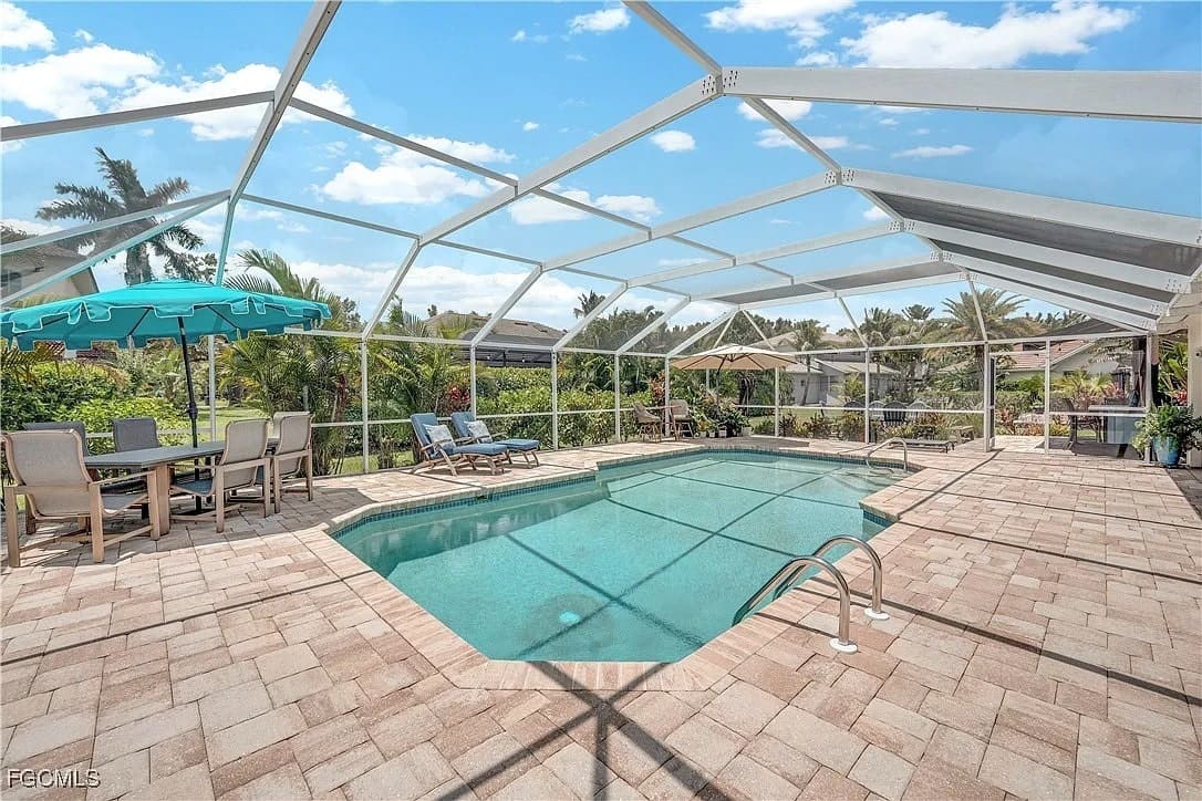 Screened-in patio with a swimming pool, lounge chairs, and outdoor dining area under a blue sky.